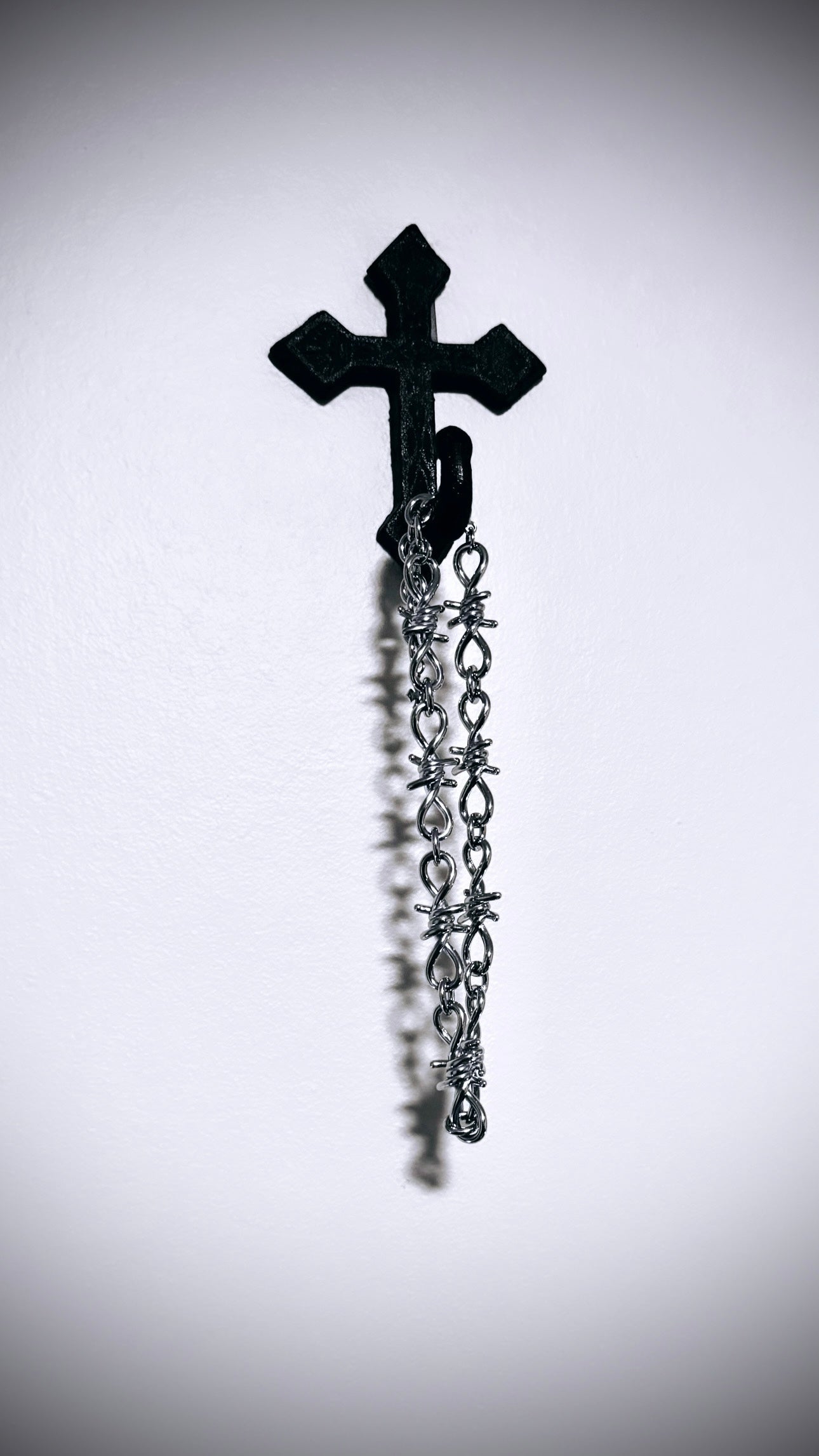 Full barbed wire necklace hanging from cross on wall
