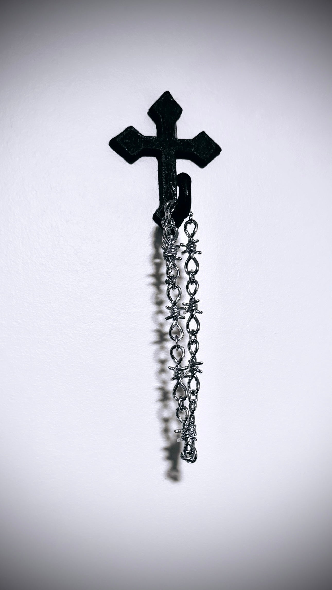 Full barbed wire necklace hanging from cross on wall 